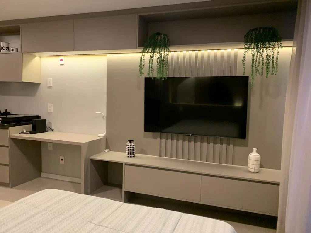Studio com bancada de home office e painel de TV